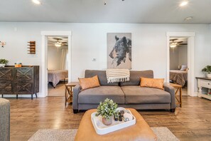A living room with a grey sofa, a wooden coffee table with a plant, and a painting on the wall.