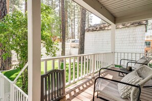 A covered porch with white railings, a seating area with wicker furniture, and a view of a white building and trees.