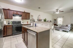 A modern kitchen with a central island, stainless steel appliances, and a dining area with a sofa and a ceiling fan. - 3 Mi to Dtwn! Houston Family Haven w/ Private Yard (Houston)