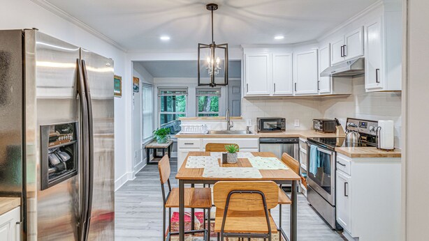 A modern kitchen with a stainless steel refrigerator, wooden dining table, and white cabinetry. - Peaceful Family Home Near Main St! (Franklinton)