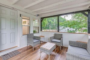 A room with a white door, two wicker chairs with cushions, a small wooden table, and a large window with a view of trees and houses. - Peaceful Family Home Near Main St! (Franklinton)