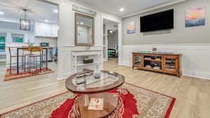A modern living room with a round coffee table, a dining area with chairs, a kitchen in the background, and a large flat-screen TV mounted on the wall. - Peaceful Family Home Near Main St! (Franklinton)
