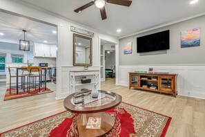 A modern living room with a round coffee table, a dining area with chairs, a kitchen in the background, and a large flat-screen TV mounted on the wall. - Peaceful Family Home Near Main St! (Franklinton)
