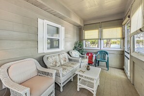 Eine überdachte Veranda mit Korbmöbeln, einem Fenster mit Jalousien und Blick ins Freie.
