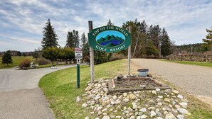 A sign for a golf resort with a mountainous landscape illustration, a slow watch sign, and a gravel path. - Top of the World Townhome w/ Views in Lake George! (Lake George)