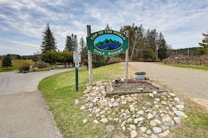 Schild für einen Golfurlaubsort mit einer Illustration einer Berglandschaft, einem Schild für eingeschränktes Tempo und einem Schotterweg.