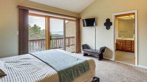 A bedroom with a bed, a TV, a balcony, and a bathroom visible through an open door. - Top of the World Townhome w/ Views in Lake George! (Lake George)