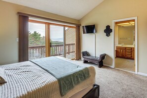 Ein Schlafzimmer mit Bett, Fernseher, Balkon und einem durch eine offene Tür sichtbaren Badezimmer.