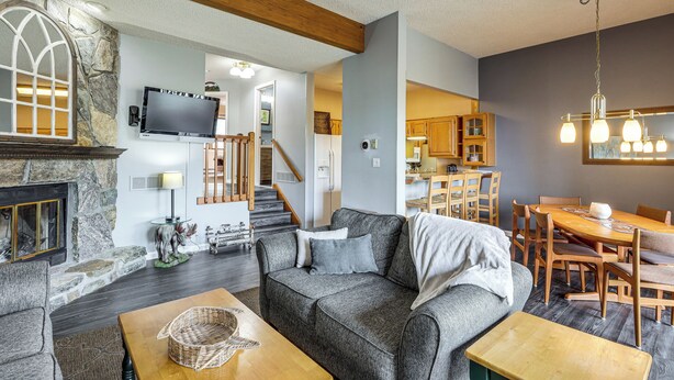 A living room with a fireplace, a sofa, a coffee table, and a dining area with a table and chairs. - Top of the World Townhome w/ Views in Lake George! (Lake George)