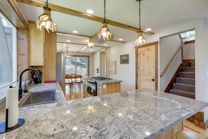 Una cocina con encimeras de granito, armarios de madera e iluminación colgante.