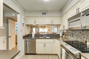 A modern kitchen with white cabinets, stainless steel appliances, and a tiled backsplash. - West End PCB: Partial Gulf Views | Steps to Beach (Panama City Beach)