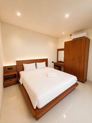 Una habitación de hotel moderna con una cama grande, cabecero de madera, mesitas de noche, un armario y un equipo de aire acondicionado.