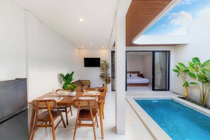 A modern dining area with a pool, a bedroom with a sliding door, and a TV mounted on the wall. - Villa Didi by Sedana Cottage (Badung)