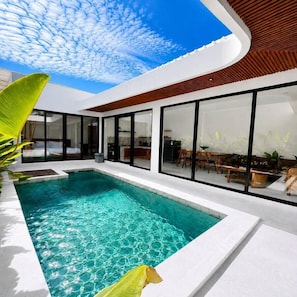 A modern pool area with a clear blue sky and a curved wooden ceiling. - Villa Didi by Sedana Cottage (Badung)