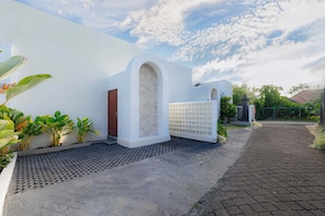 A modern building with a white exterior, a brick entrance, and a paved pathway leading to a gated area. - Villa Didi by Sedana Cottage (Badung)