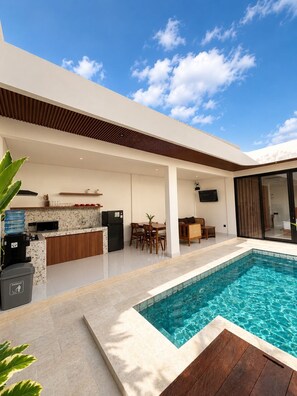Un espacio exterior moderno con piscina, cocina y comedor.
