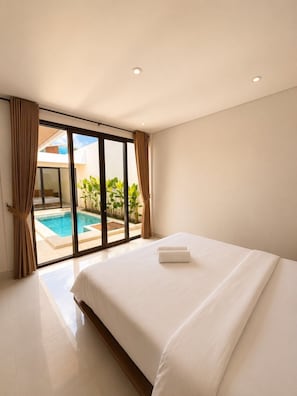 A hotel room with a large bed, a sliding glass door leading to a pool area, and a view of the outdoors. - Sedana Villa (Badung)
