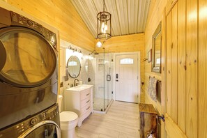A wooden interior with a washing machine, sink, mirror, and glass shower.