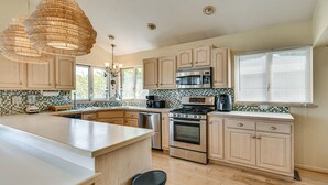 Een keuken met een groot eiland, roestvrijstalen apparatuur, houten kastjes en een betegelde spatwand.