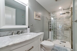 Une salle de bain avec un lavabo en marbre, des toilettes, une douche en verre et un tableau encadré au mur.