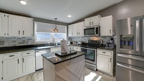 A modern kitchen with white cabinets, a central island, stainless steel appliances, and a window providing natural light.