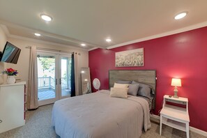 Une chambre à coucher comprenant un lit, une table de chevet, un téléviseur et une porte-fenêtre coulissante donnant sur un espace extérieur.