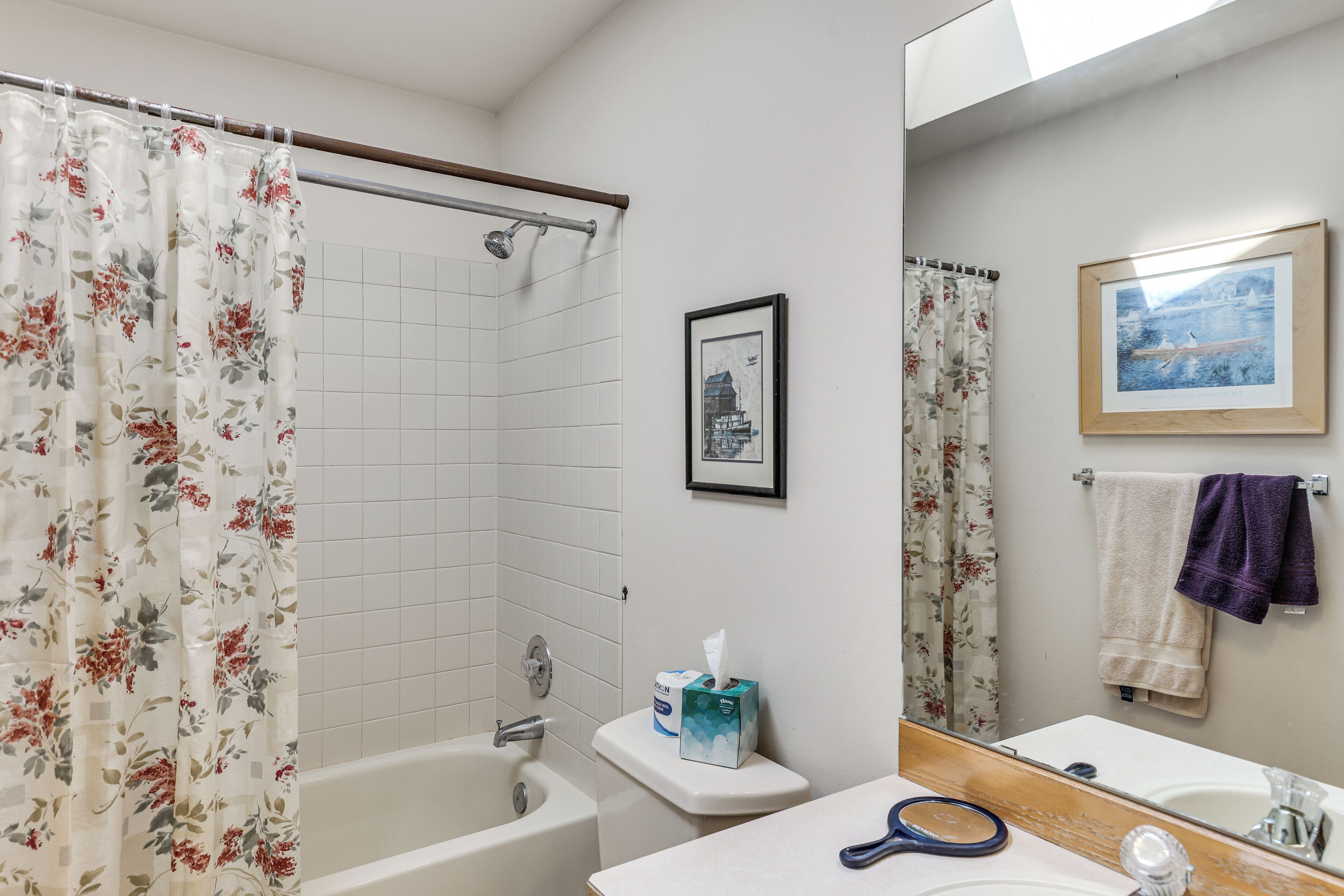 A bathroom with a shower, toilet, sink, and a framed picture on the wall.