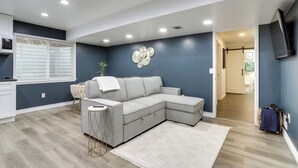 Un salon comprenant un canapé d’angle, une petite table d’appoint, un élément décoratif mural et un téléviseur fixé au mur.