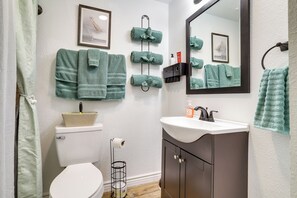 Une salle de bain équipée de toilettes, d’un lavabo, d’un miroir, d’un porte-serviettes et de tableaux encadrés accrochés au mur.