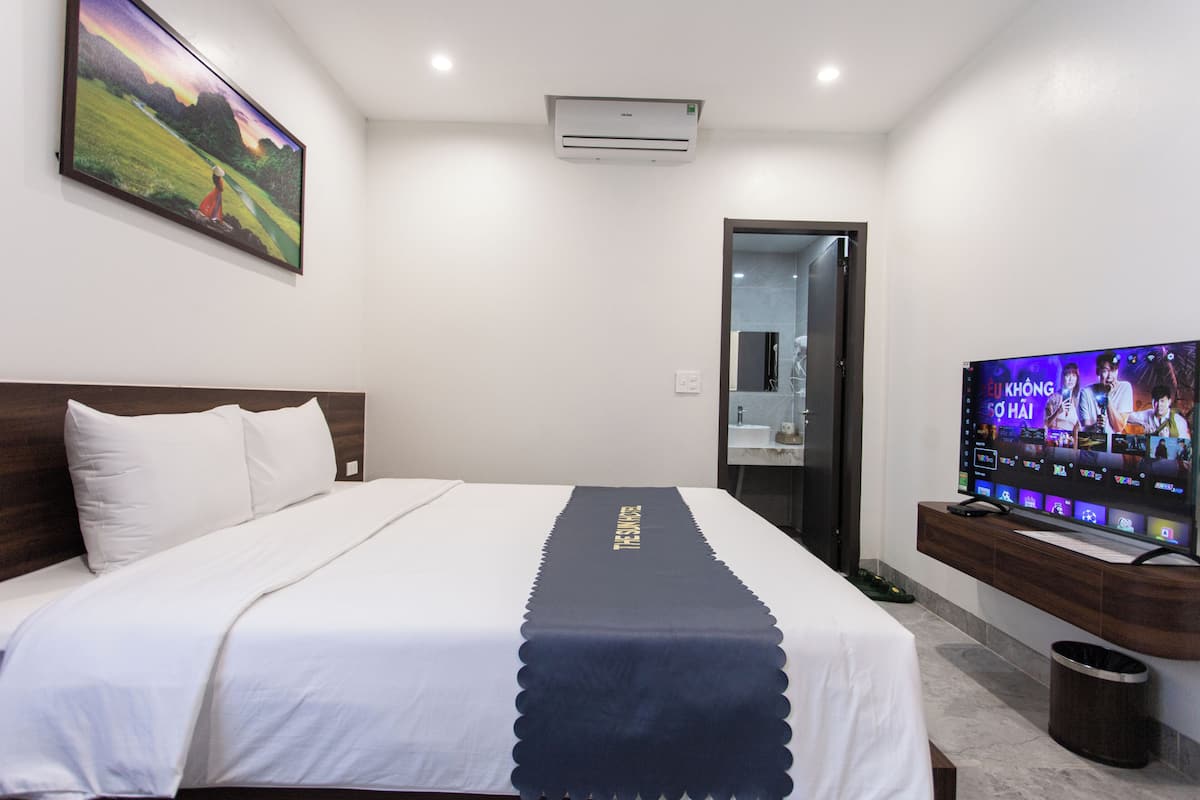 A hotel room with a bed, a television, an air conditioner, and a painting on the wall.
