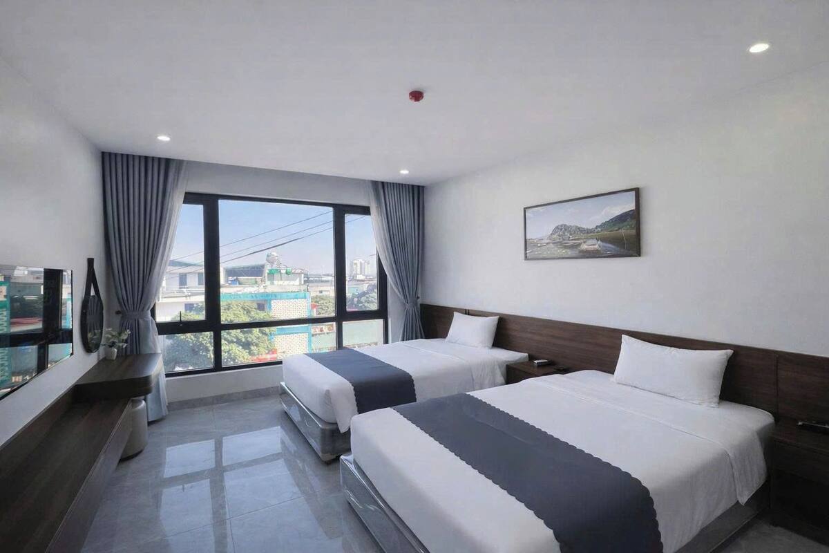 A hotel room with two beds, a large window with curtains, a flat-screen TV, and a painting on the wall.
