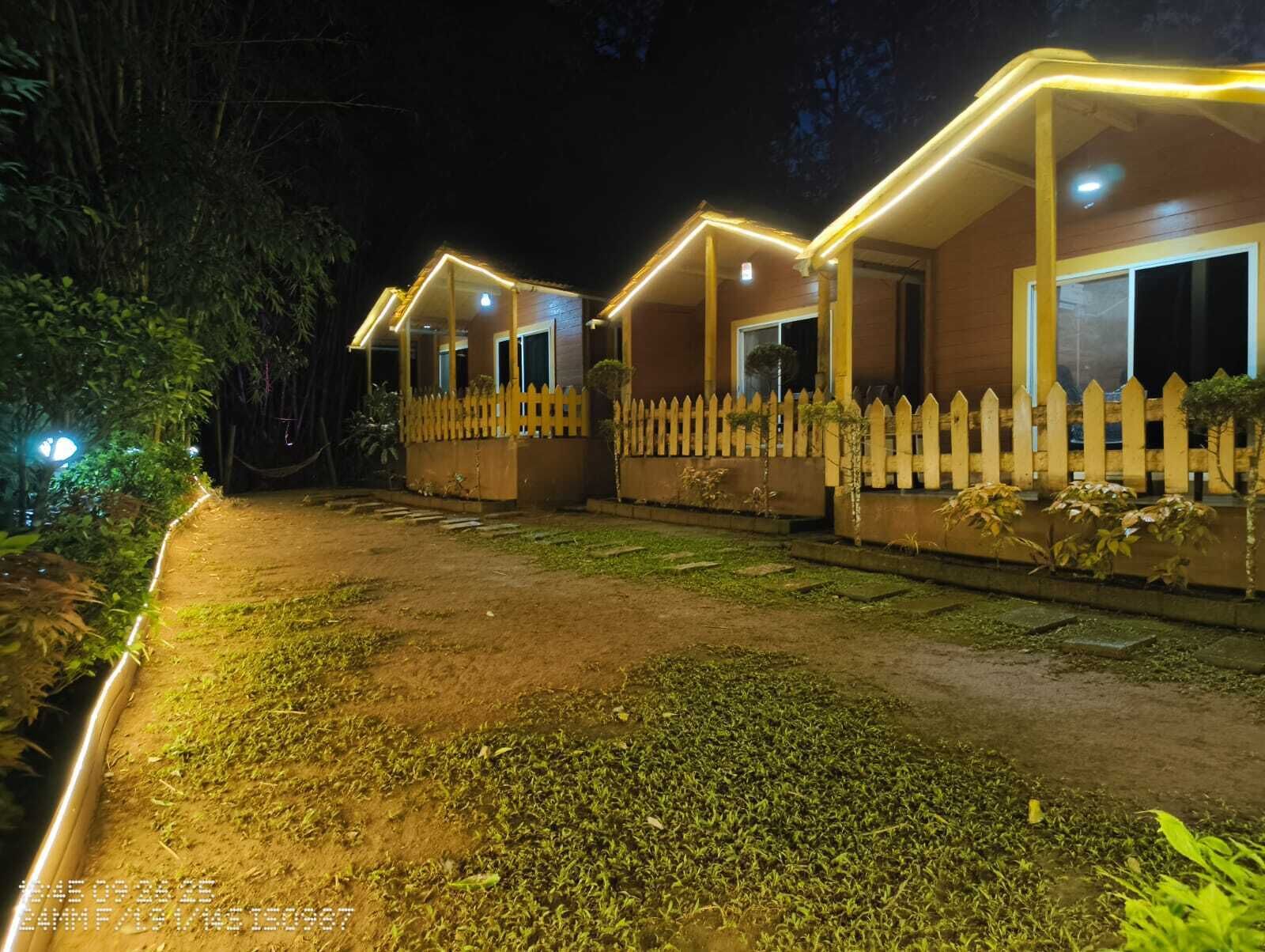 A row of wooden cabins with white picket fences, illuminated by warm lighting.