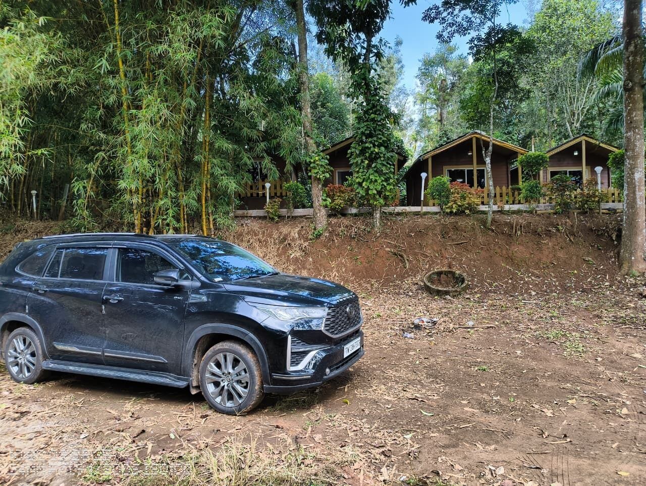A black SUV parked on a dirt path with wooden cabins in the background.