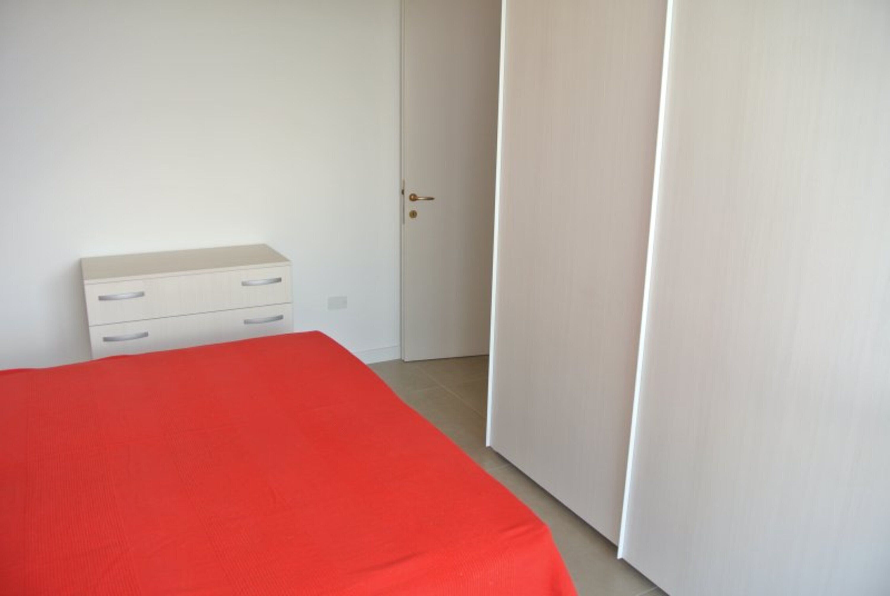 Een slaapkamer met een bed, een witte ladekast en een deur.