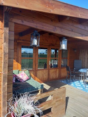 Eine Holzhütte mit Veranda, Esstisch und einer Couch mit Kissen.