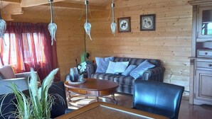 A wooden interior with a dining table, chairs, a sofa, and hanging crystal chandeliers.