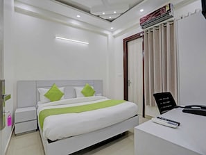A modern hotel room with a bed, bedside tables, a desk with a phone and remote, and an air conditioning unit. - The Vertigo (Noida)