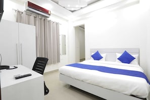 A hotel room with a bed, a desk, a chair, a telephone, and an air conditioning unit. - The Vertigo (Noida)