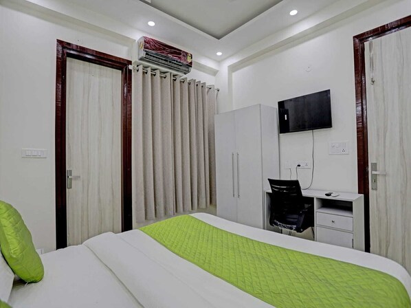 A hotel room with a bed, a desk, a TV, and an air conditioning unit. - The Vertigo (Noida)
