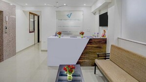 A hotel reception area with a reception desk, a seating area, and a wall-mounted TV. - The Vertigo (Noida)