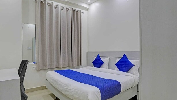 A hotel room with a bed, a chair, a curtain, and a wall-mounted light fixture. - The Vertigo (Noida)