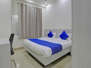 A hotel room with a bed, a chair, a curtain, and a wall-mounted light fixture. - The Vertigo (Noida)