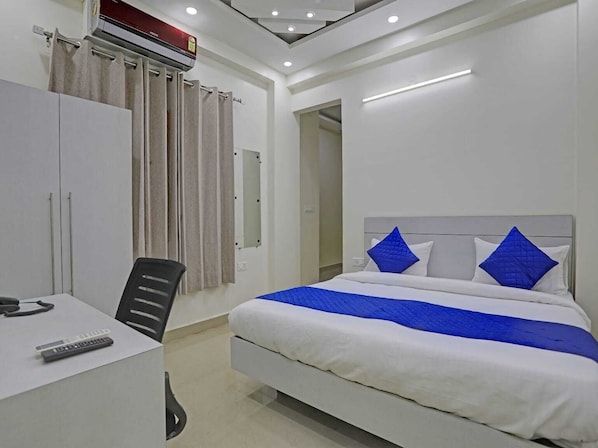 A hotel room with a bed, a desk with a chair, a desk lamp, and a telephone. - The Vertigo (Noida)