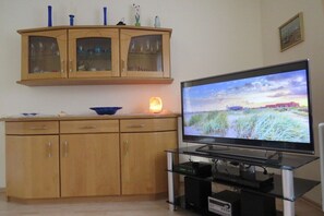A living room with a flat-screen TV, wooden cabinets, and a glass coffee table. - Holiday home in Norden with swimming pool (Norden)
