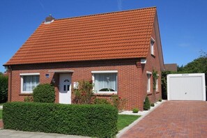A two-story brick house with a red-tiled roof, a white garage door, and a well-maintained hedge. - Holiday home in Norden with swimming pool (Norden)