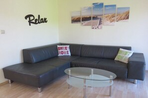 A modern living room with a sectional sofa, a glass coffee table, and three framed pictures on the wall. - Holiday home in Norden with swimming pool (Norden)