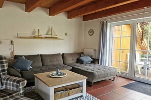 Ein gemütliches Wohnzimmer mit einer Couch, einem Couchtisch und einem Esstisch. An der Wand hängen zwei kleine dekorative Schiffe.