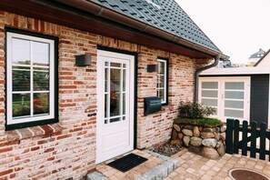Una casa de ladrillo con una puerta blanca, dos ventanas, un buzón, un muro de piedra y una valla de madera.