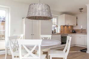 Una cocina moderna con armarios blancos, una mesa de comedor redonda y una lámpara colgante de mimbre.