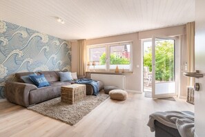 Ein Wohnzimmer mit einer Couch, einem Couchtisch, einer Wand mit Muster und Blick durch eine Glastür.